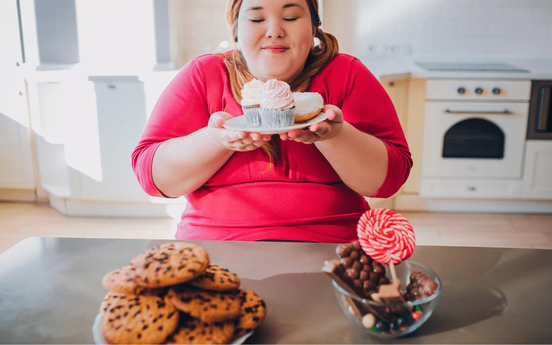Obese Girl Smiling At Cupcakes On Hand And Table Full Of Cookies Chocolates Candy