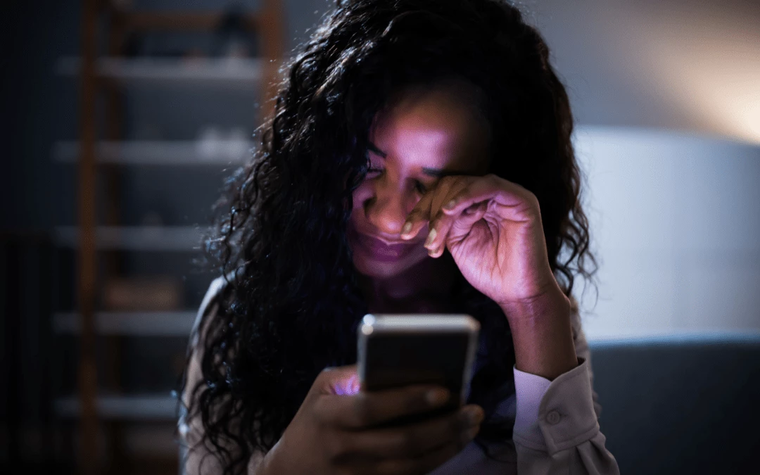 A Tired Woman Sitting In The Dark And Rubbing Her Eyes While Holding Phone On Her Hand