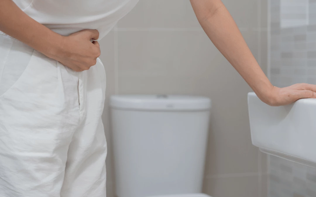 Woman Holding Onto Her Stomach Indicating Pain Standing Beside Toilet Bowl