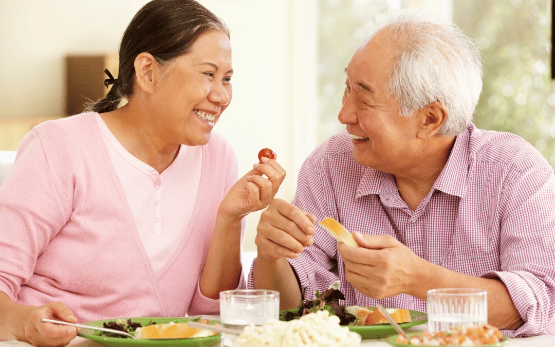 happy-elderly-couple-looking-at-each-other-and-holding-piece-of-fruits-with-table-full-of-healthy-foods-and-fruits